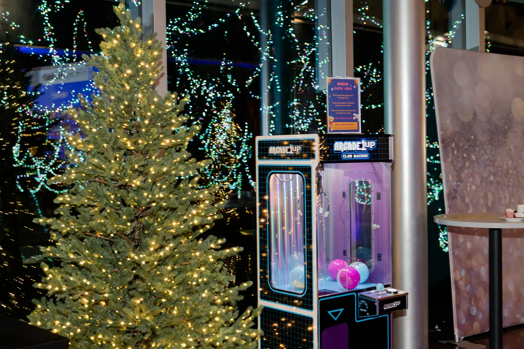 Branded claw machine filled with prize capsules beside a lit holiday tree
