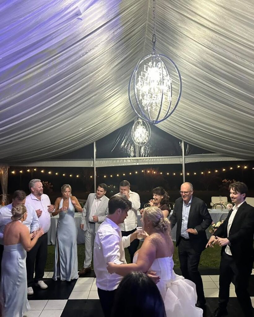 Wedding guests dancing under chandeliers in a white tent at night