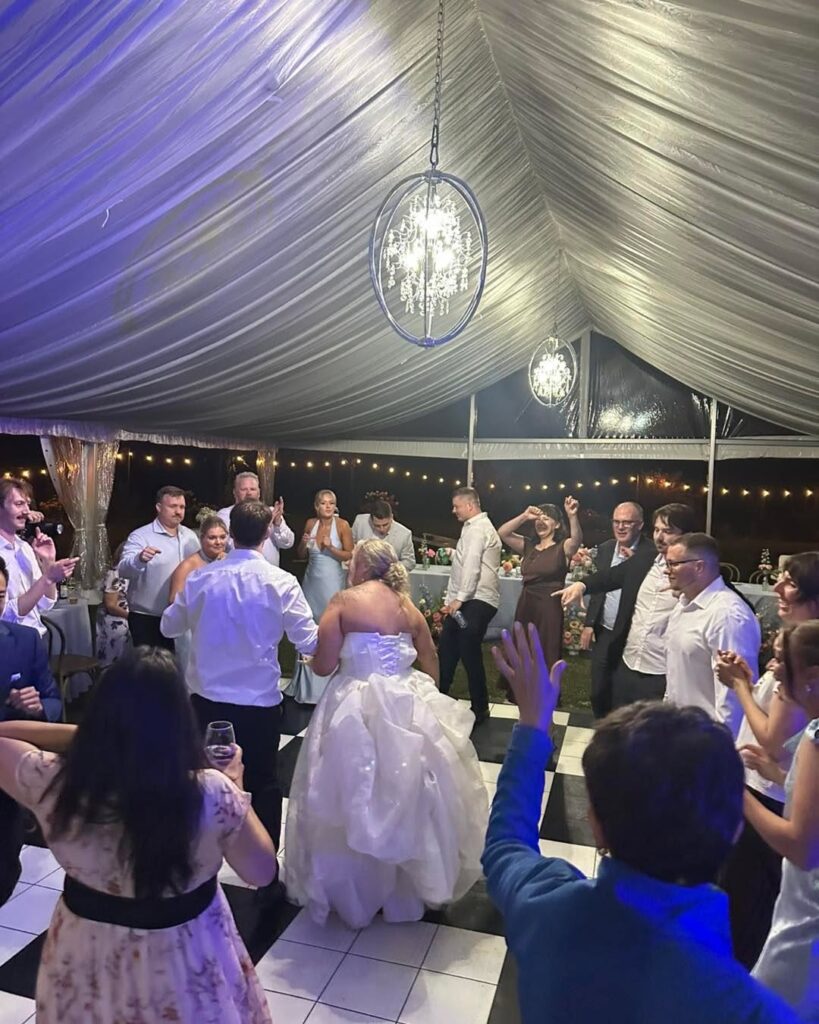 Guests circling the bride on the dance floor with string lights behind them