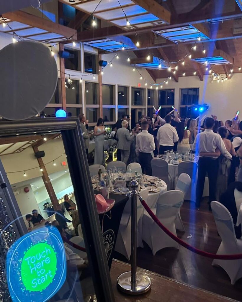 Mirror photo booth showing touch here to start, set beside a wedding reception