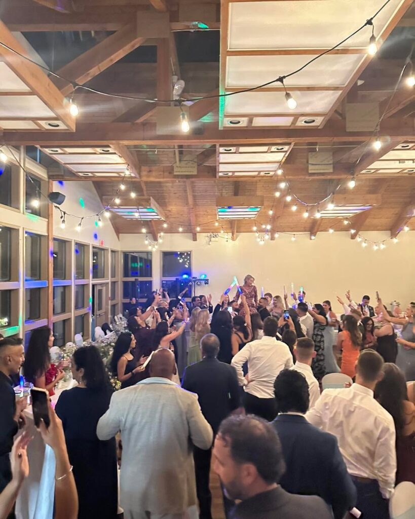 Guests dancing in a wood beam hall with blue lighting and string lights